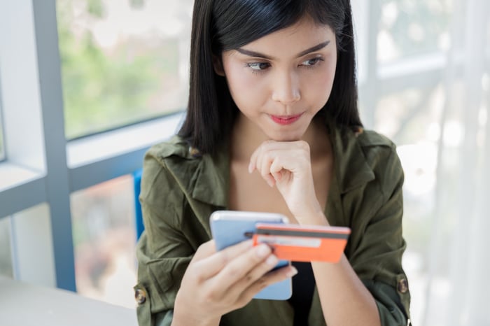 young woman holding credit card and smartphone and thinking with chin on fist