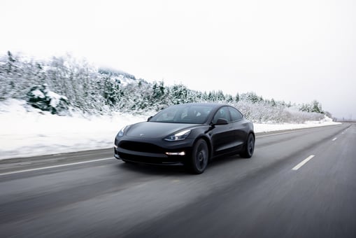 A black Tesla car driving on an open road in the snow