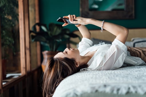 A young person laying on a bed looking at a smartphone