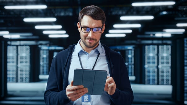 A person looking down at a tablet device while standing in a data center