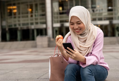woman hijabi eating apple on phone online banking