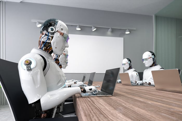 Multiple robots typing on laptops in a conference room. 