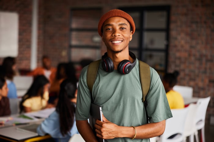 A person with a backpack and headphones around their neck holding a laptop.