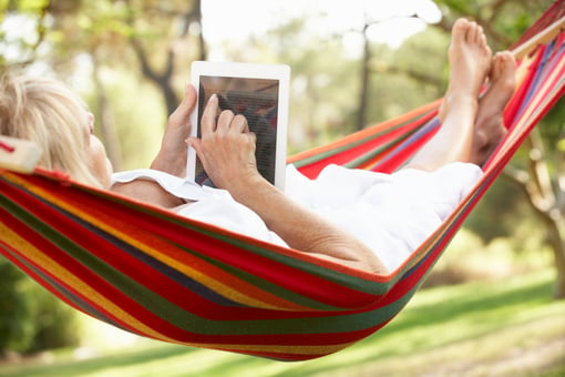 senior woman relaxing in hammock reading ebook