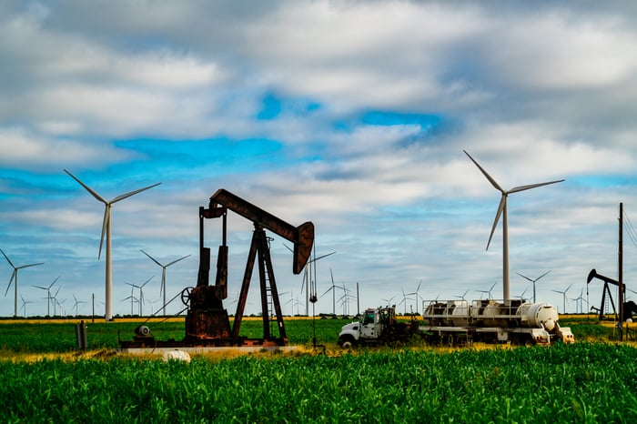 An oil well with clean energy wind turbines in the background.