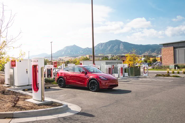 A Tesla EV parked in front of a bank of superchargers.