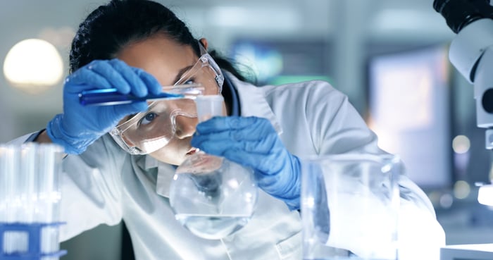 A person in a lab pouring liquid into a beaker. 