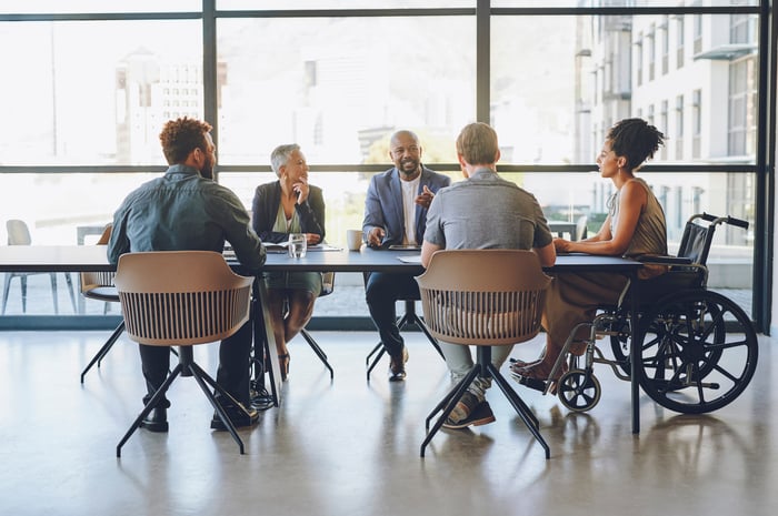 A group of people in a meeting room talking at a table.