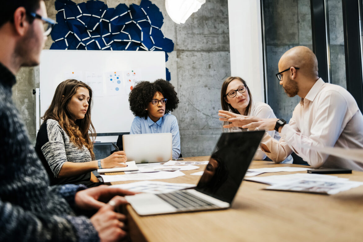 a-group-of-five-colleagues-seated-at-a-large-table-collaborating-at-work.jpg