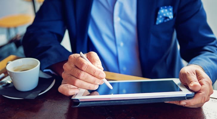 A man reviews his finances on a tablet while enjoying a coffee in a cafe. 