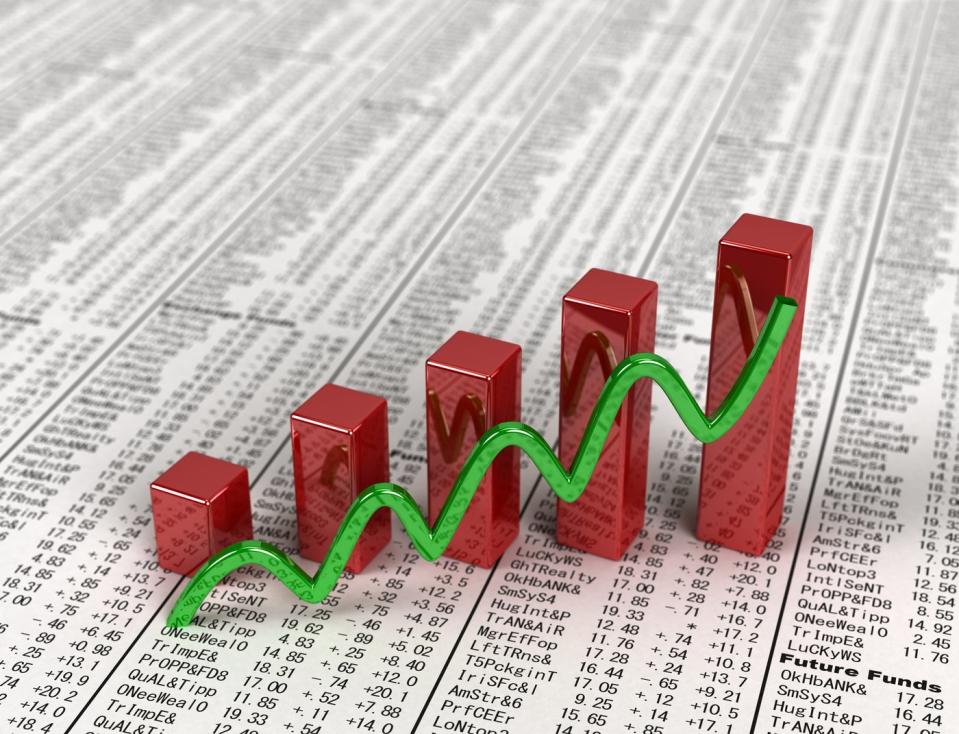 An ascending green line and rising bar chart set atop a financial newspaper with visible stock quotes.