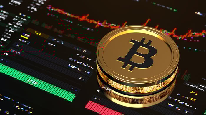 Gold Bitcoin on top of a stock market trading screen.