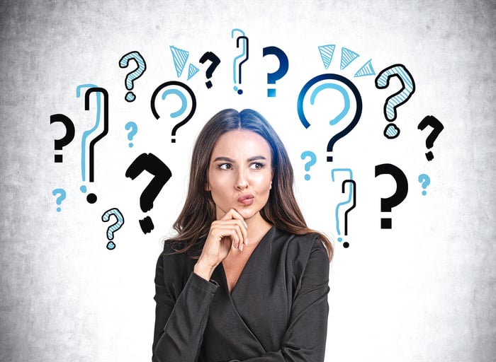 A person with their hand on their chin against a backdrop of illustrated question marks.