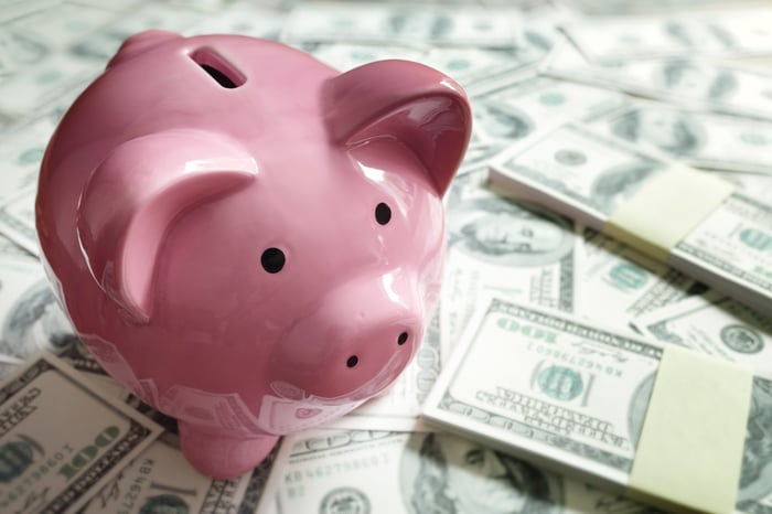 A piggy bank sitting on top of stacks of hundred dollar bills.