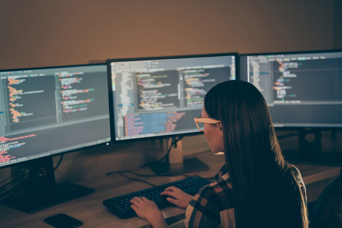 a-person-sitting-at-a-desk-with-multiple-computer-monitors-writing-code.jpg