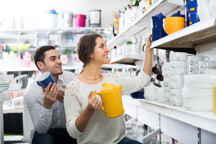 Two people selecting teapots and cups from a store shelf. 