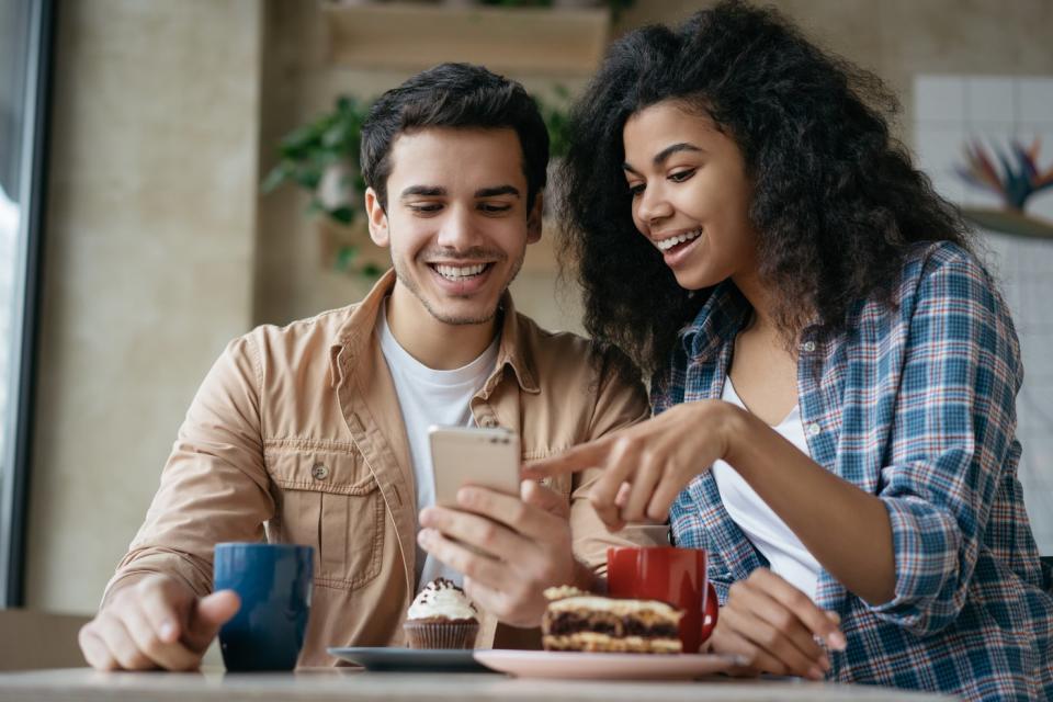 Two people having lunch at home look at something on a phone.