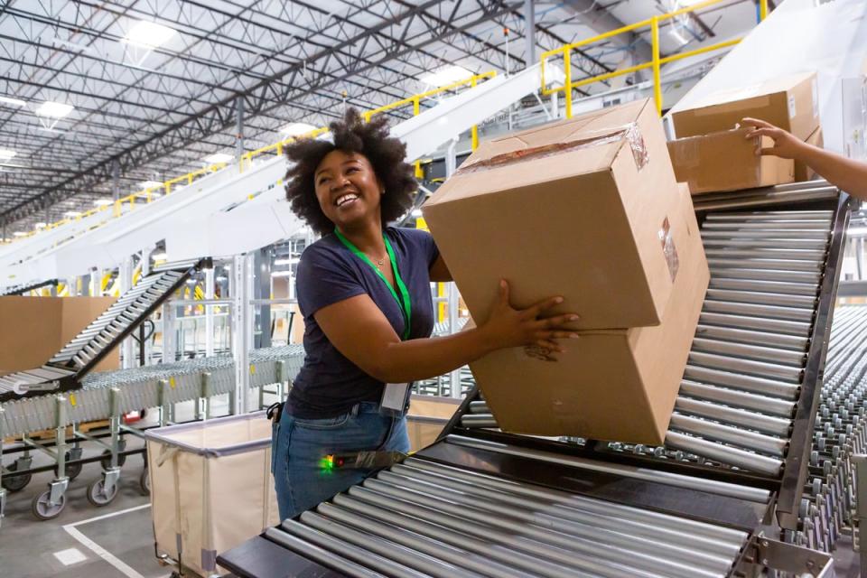 A person smiles while taking packages off of a conveyor in a warehouse.