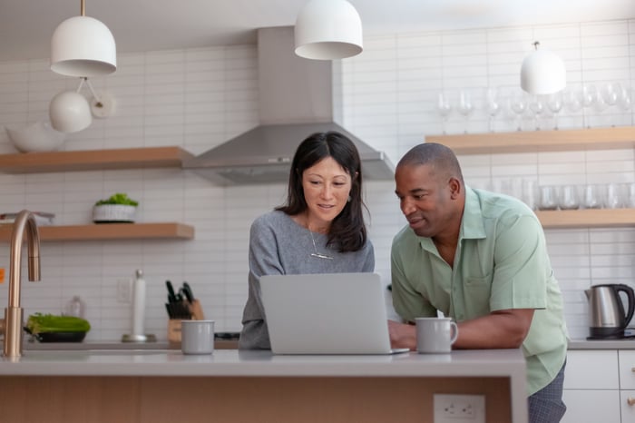 Two people looking at a laptop on a kitchen island.