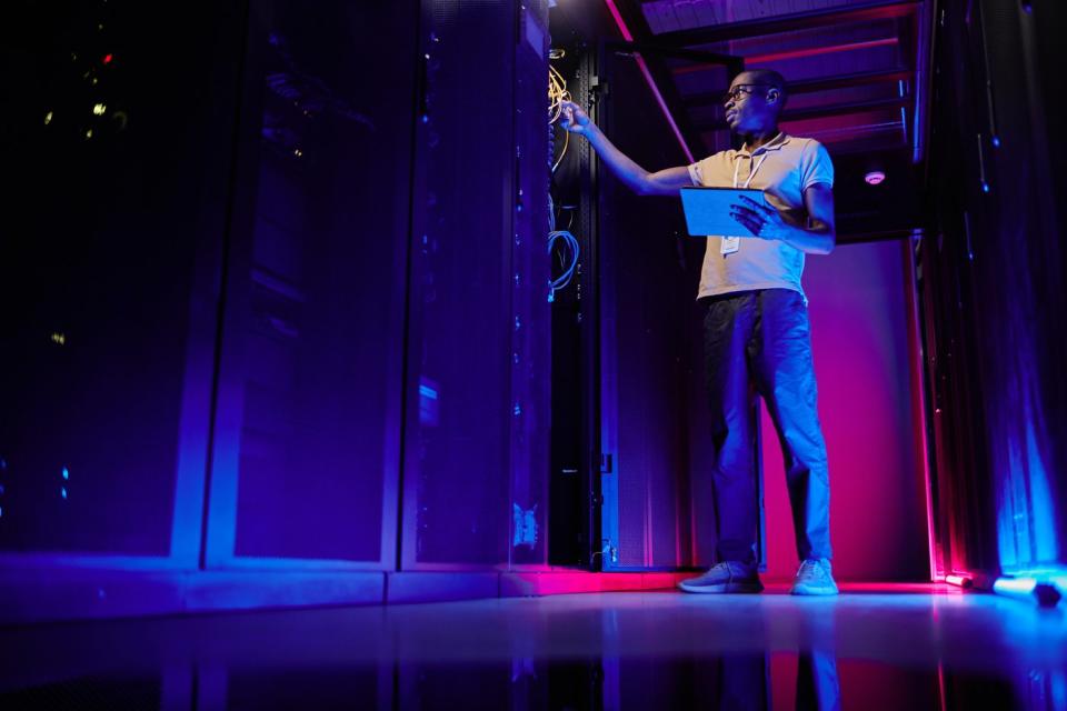 A system administrator setting up server network in a data center lit by neon light.
