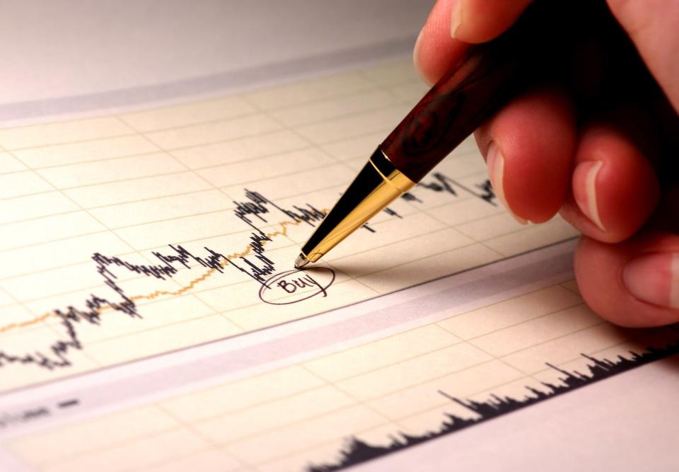 A person writing and circling the word, buy, beneath a dip in a stock chart.