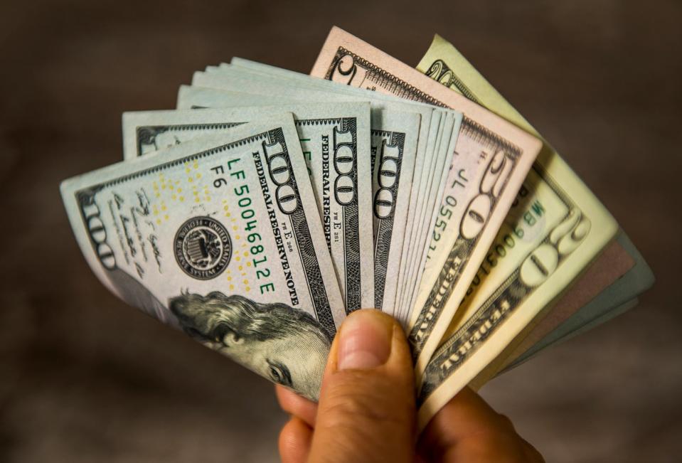 A person holding an assortment of fanned and folded cash bills by their fingertips.